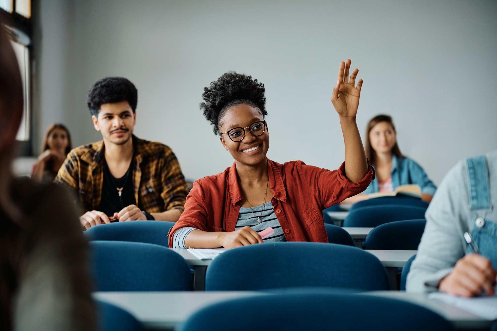 Happy black student raising her hand to ask a question during a class at the university.